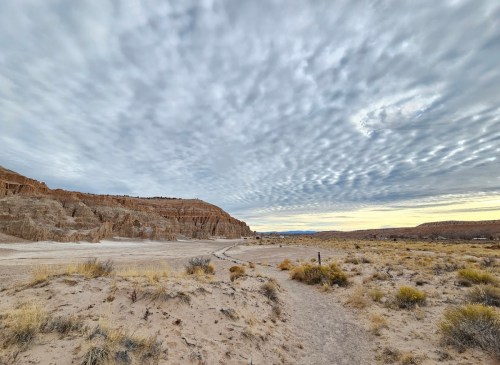 A vast desert landscape with rugged cliffs, a winding path, and a cloudy sky overhead.