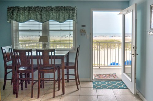 Bright beachside dining area with a table and chairs, open door leading to a balcony with ocean views.