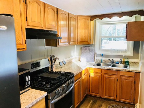 Cozy kitchen with wooden cabinets, granite countertops, a gas stove, and a window overlooking a snowy landscape.