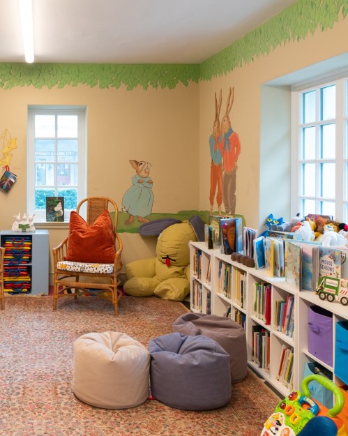 Cozy children's library with colorful bookshelves, bean bags, and whimsical wall art of rabbits.