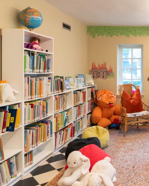 A cozy children's reading nook with bookshelves, plush toys, and colorful seating in a bright, inviting room.