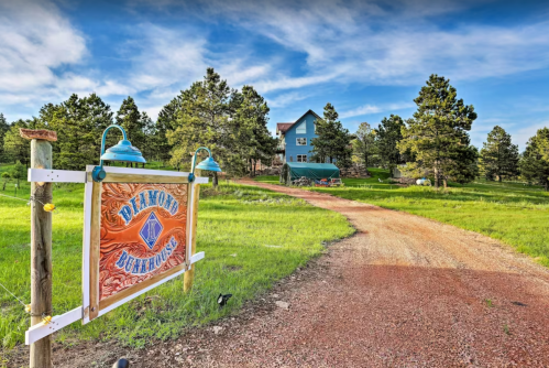 A scenic view of a dirt road leading to a blue house, with a sign for "Diamond Bunkhouse" surrounded by greenery.