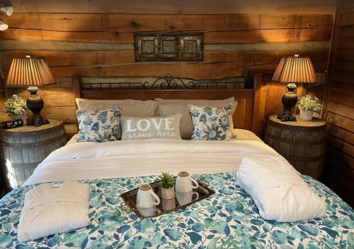 Cozy bedroom with a wooden wall, a bed adorned with floral bedding, and decorative lamps on barrel nightstands.