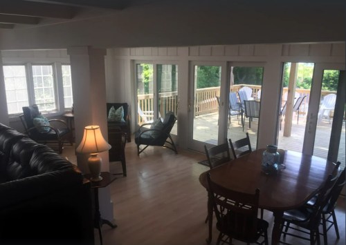 Bright, airy living space with a dining table, chairs, and large windows leading to a deck with outdoor seating.