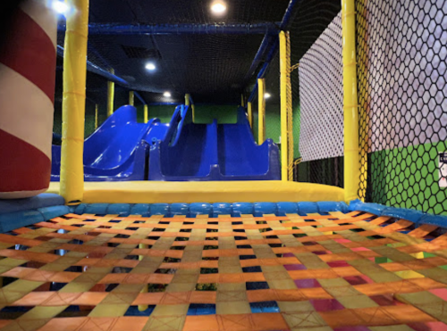 Colorful indoor playground featuring blue slides and a safety netted area with a soft, woven floor.