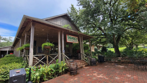 A rustic restaurant with a wooden exterior, surrounded by greenery and brick pathways, under a blue sky.