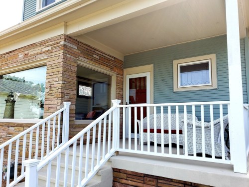 A porch with white railings, a wicker chair, and a blue house exterior featuring stone accents.