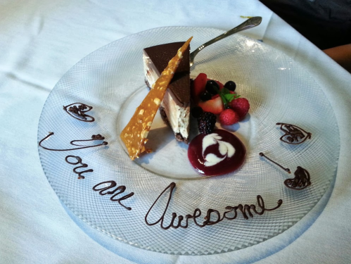 A dessert plate featuring a chocolate cake slice, berries, and a message written in chocolate: "You are Awesome."