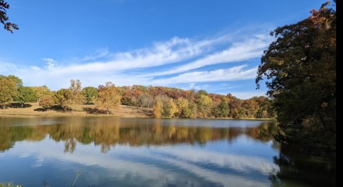 A serene lake surrounded by autumn trees, reflecting colorful foliage under a clear blue sky.