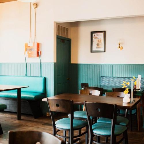 Cozy café interior with teal accents, wooden tables, and chairs, featuring a flower vase and framed artwork on the wall.