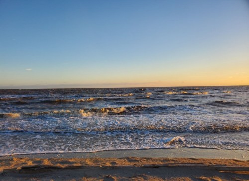 A serene beach scene at sunset, with gentle waves lapping at the shore under a colorful sky.
