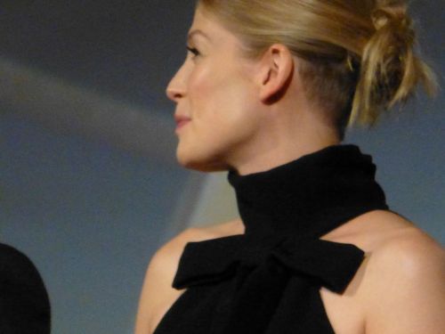 A woman with blonde hair styled in a bun, wearing a black sleeveless top with a bow, looking to the side.