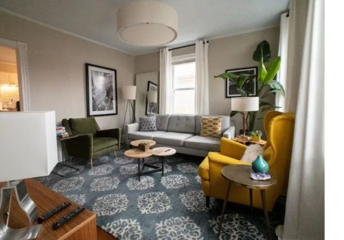 A cozy living room with a gray sofa, yellow armchair, green chair, and decorative plants, featuring a patterned rug.