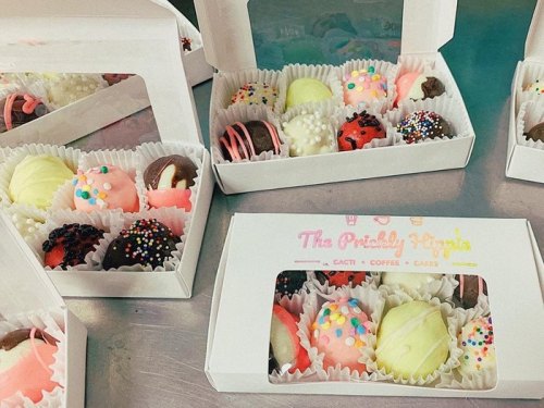 A variety of colorful, decorated chocolates in white boxes, featuring sprinkles and different flavors.