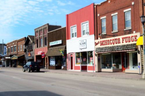 A quaint street lined with shops, including a fudge store, under a clear blue sky.