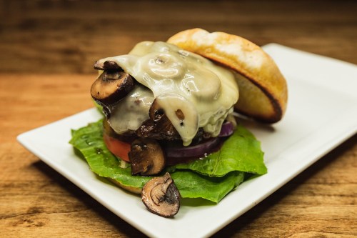 A juicy burger topped with melted cheese, mushrooms, lettuce, tomato, and onion, served on a toasted bun.