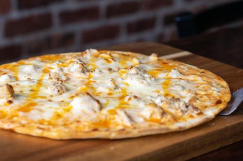 A freshly baked pizza with melted cheese and chunks of chicken on a wooden serving board.