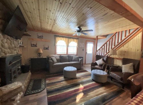 Cozy living room with wooden ceiling, stone fireplace, comfortable seating, and colorful area rug.
