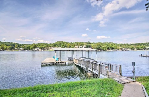 A serene lake view with a wooden dock extending into the water, surrounded by green hills and a clear blue sky.