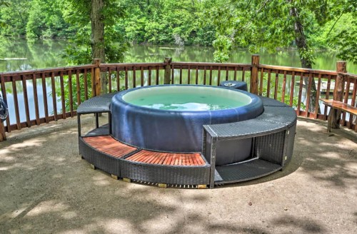 A hot tub on a wooden deck overlooking a serene river surrounded by lush greenery.