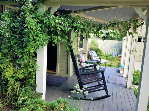 A cozy porch with a rocking chair, surrounded by greenery and flowers, inviting relaxation in a peaceful setting.