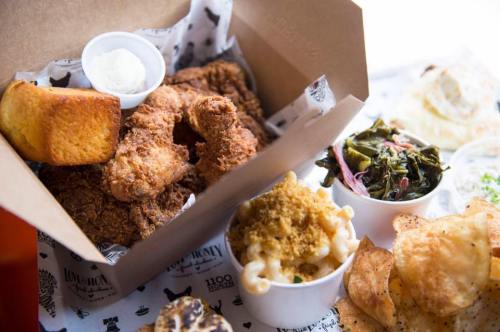 A takeout box filled with fried chicken, cornbread, macaroni and cheese, collard greens, and potato chips.