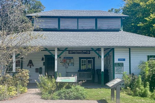 A white building with green accents, featuring signs for the Appalachian Trail and surrounded by trees and flowers.