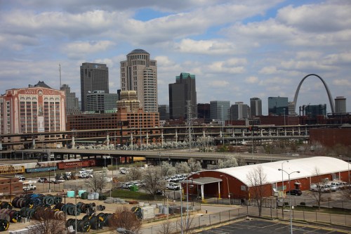 View of St. Louis skyline featuring the Gateway Arch, with industrial areas and cloudy skies in the foreground.