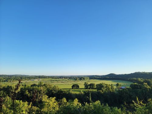 A panoramic view of a lush green landscape under a clear blue sky, with rolling hills in the distance.