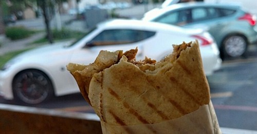 A partially eaten wrap in the foreground with cars parked in the background.