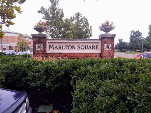 Sign for Marlton Square surrounded by greenery, with decorative planters on either side.