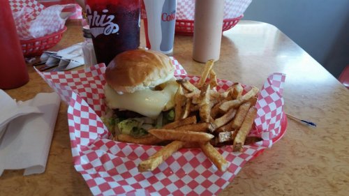 A burger with melted cheese and lettuce, served with a side of fries in a red-checkered basket.