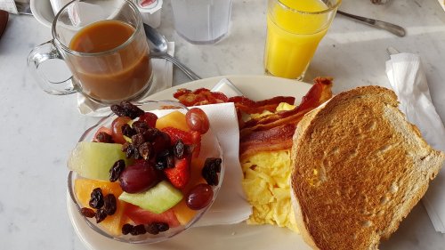 A breakfast plate with scrambled eggs, toast, bacon, and a fruit bowl, alongside coffee and orange juice.