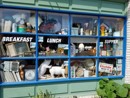 A colorful window display featuring various vintage items and signs for breakfast, lunch, and supper.