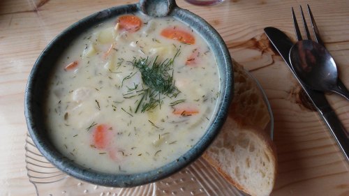 A bowl of creamy soup with carrots and herbs, served with slices of bread on a wooden table.