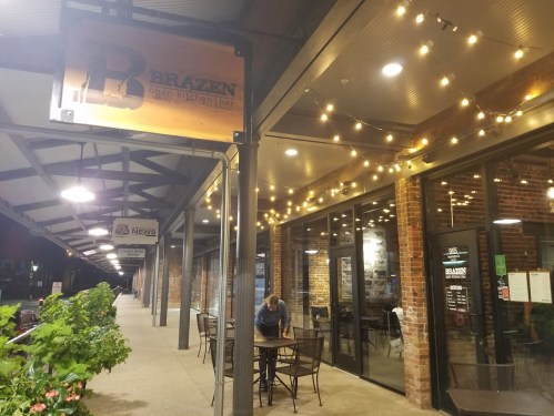Exterior of Brazen Open Kitchen Bar with string lights, tables outside, and a person setting up for the evening.
