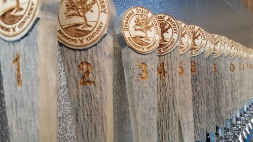 A row of wooden tap handles with engraved numbers and circular brewery logos, showcasing a selection of beers.
