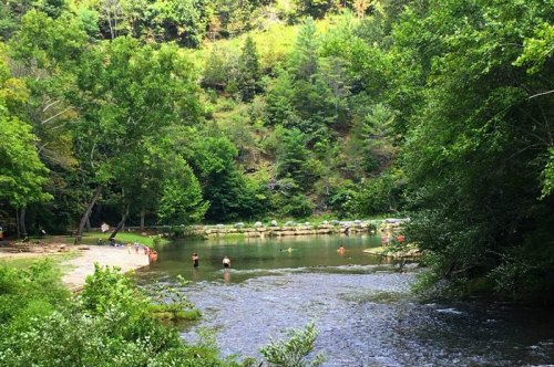 A serene river scene surrounded by lush greenery, with people swimming and relaxing along the water's edge.