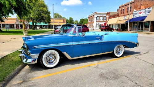 A classic blue convertible car parked on a sunny street with shops in the background.