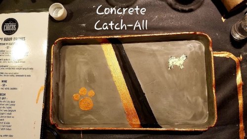 A decorative concrete catch-all tray with a gold stripe, a paw print, and a small dog silhouette.