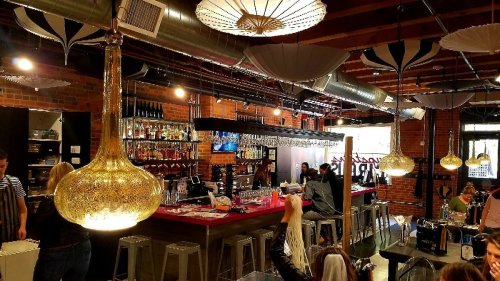 A stylish bar interior with pendant lights, a brick wall, and patrons enjoying drinks in a vibrant atmosphere.