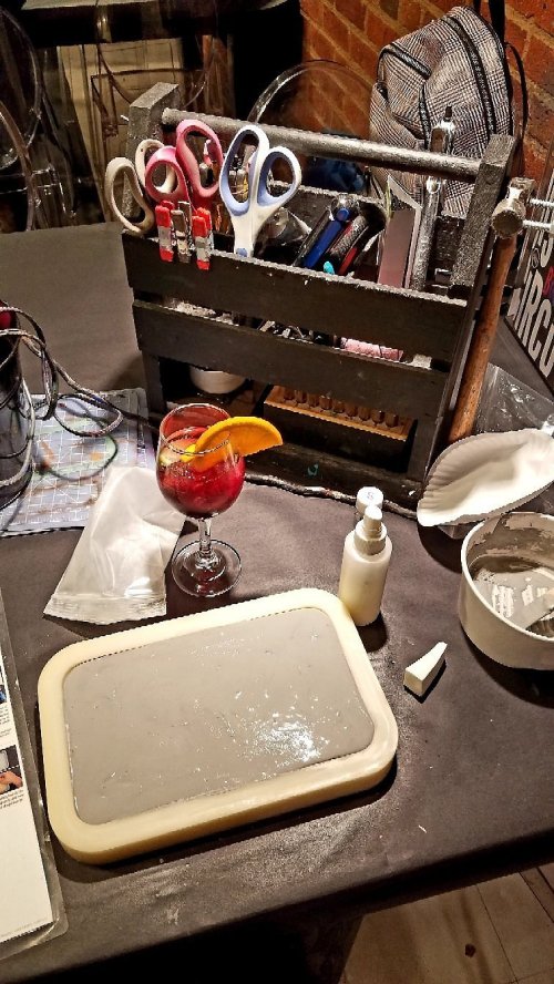 A table with a cocktail garnished with an orange slice, a gray tray, scissors, and various tools in a wooden crate.