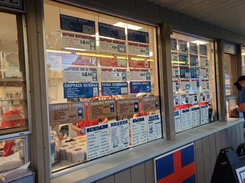 Menu boards displayed in a window, featuring various food items and prices at a seaside eatery.