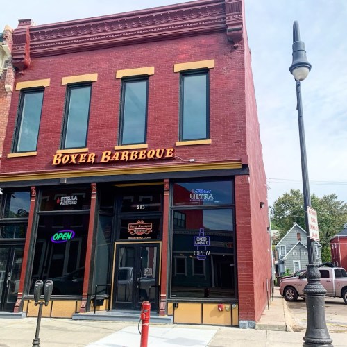 Exterior of Boxer Barbeque, a red brick building with large windows and an "Open" sign, on a sunny day.