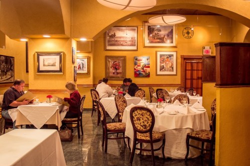 Elegant restaurant interior with tables set for dining, featuring artwork on the walls and soft lighting.