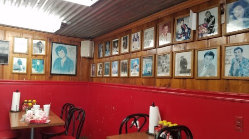 A cozy diner interior with red walls, wooden paneling, and framed black-and-white photos on the wall. Tables with condiments.