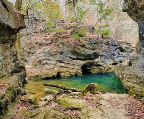 A serene natural scene featuring a clear blue pool surrounded by rocky cliffs and autumn foliage.