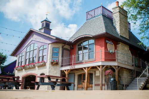 Charming building with a mix of stone and colorful facades, featuring outdoor seating and decorative flowers.