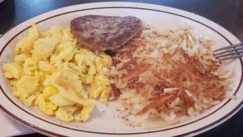 A plate of scrambled eggs, a sausage patty, and crispy hash browns.