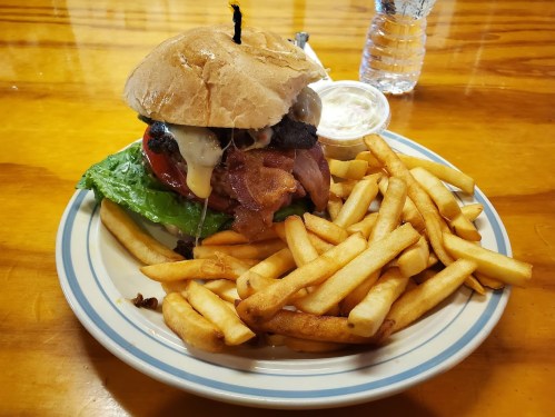 A hearty burger with lettuce, tomato, and cheese, served with a side of golden fries on a blue and white plate.